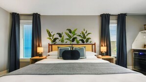 Une chambre d’hôtel avec un grand lit, deux tables de chevet avec des lampes, une composition florale décorative et une vue sur la ville par la fenêtre.