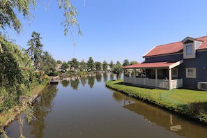 A calm river with a house on the right, a dock on the left, and a clear blue sky.