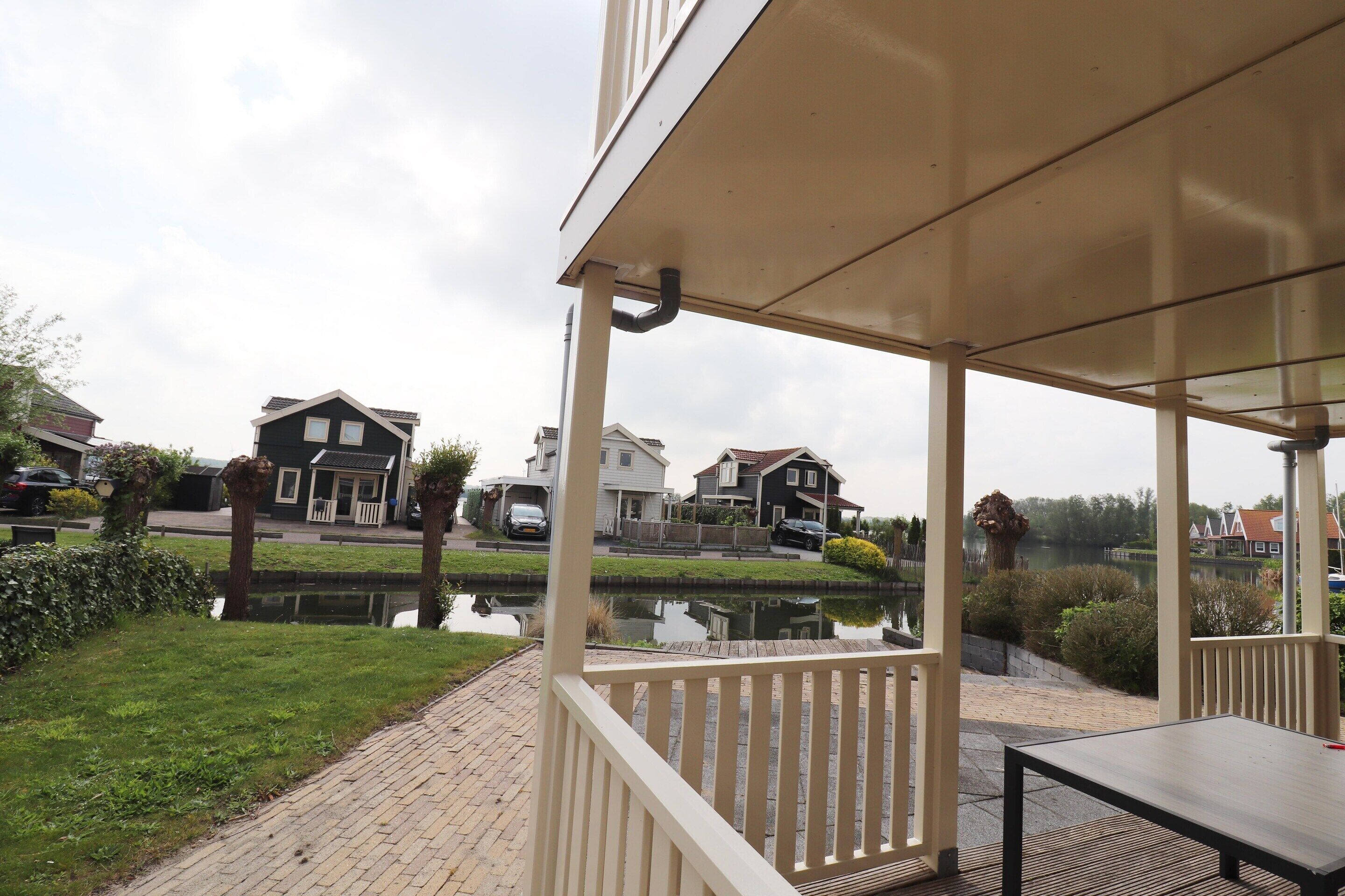 A covered outdoor area with a table and chairs, a pond, and houses in the background.