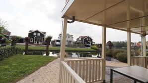 A covered outdoor area with a table and chairs, a pond, and houses in the background.