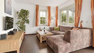 A living room with a sofa, a coffee table, a TV, and a plant.