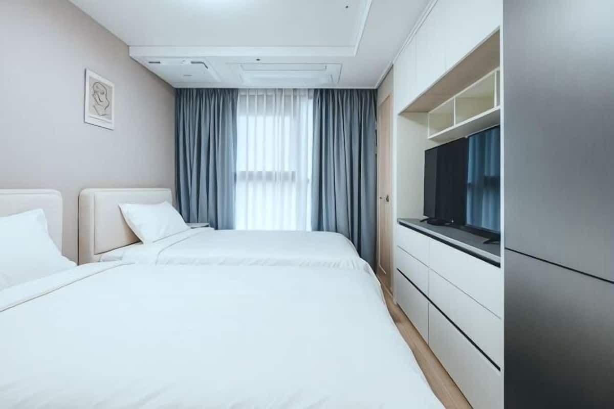 A hotel room with a bed, a television, a window with curtains, and a door.