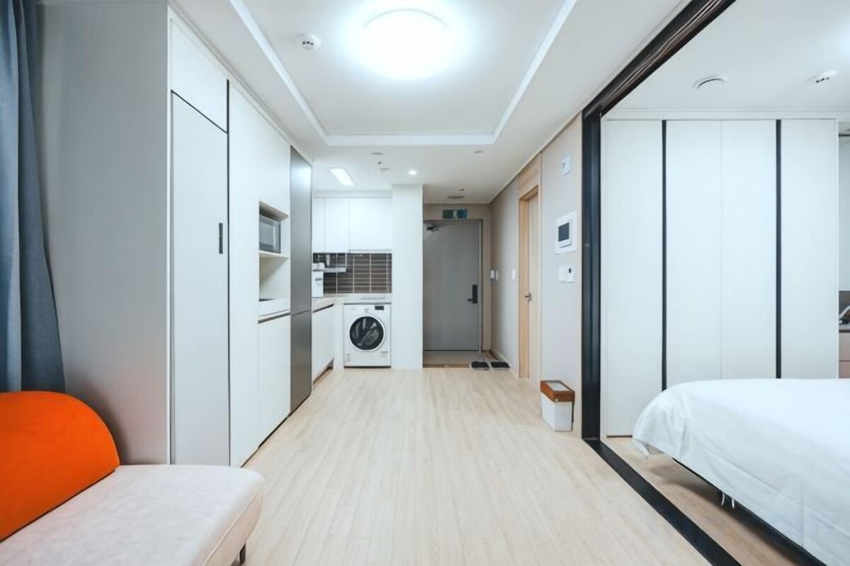 A hotel room with a bed, a sofa, a kitchenette, and a laundry area.