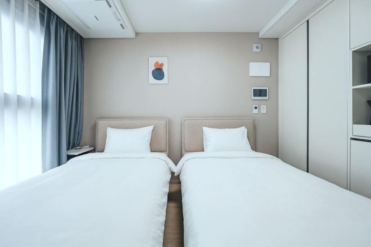 Ett hotellrum med två sängar, ett nattduksbord, en väggmonterad TV och ett fönster med gardiner.