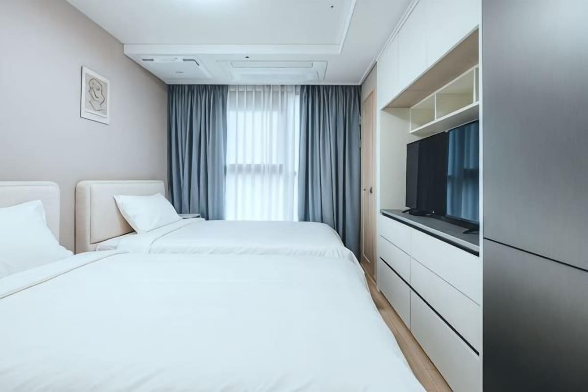 A hotel room with a bed, a television, a window with curtains, and a door.