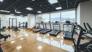 Een sportschool met loopbanden, krachtapparaten en een groot raam met uitzicht op de stad.