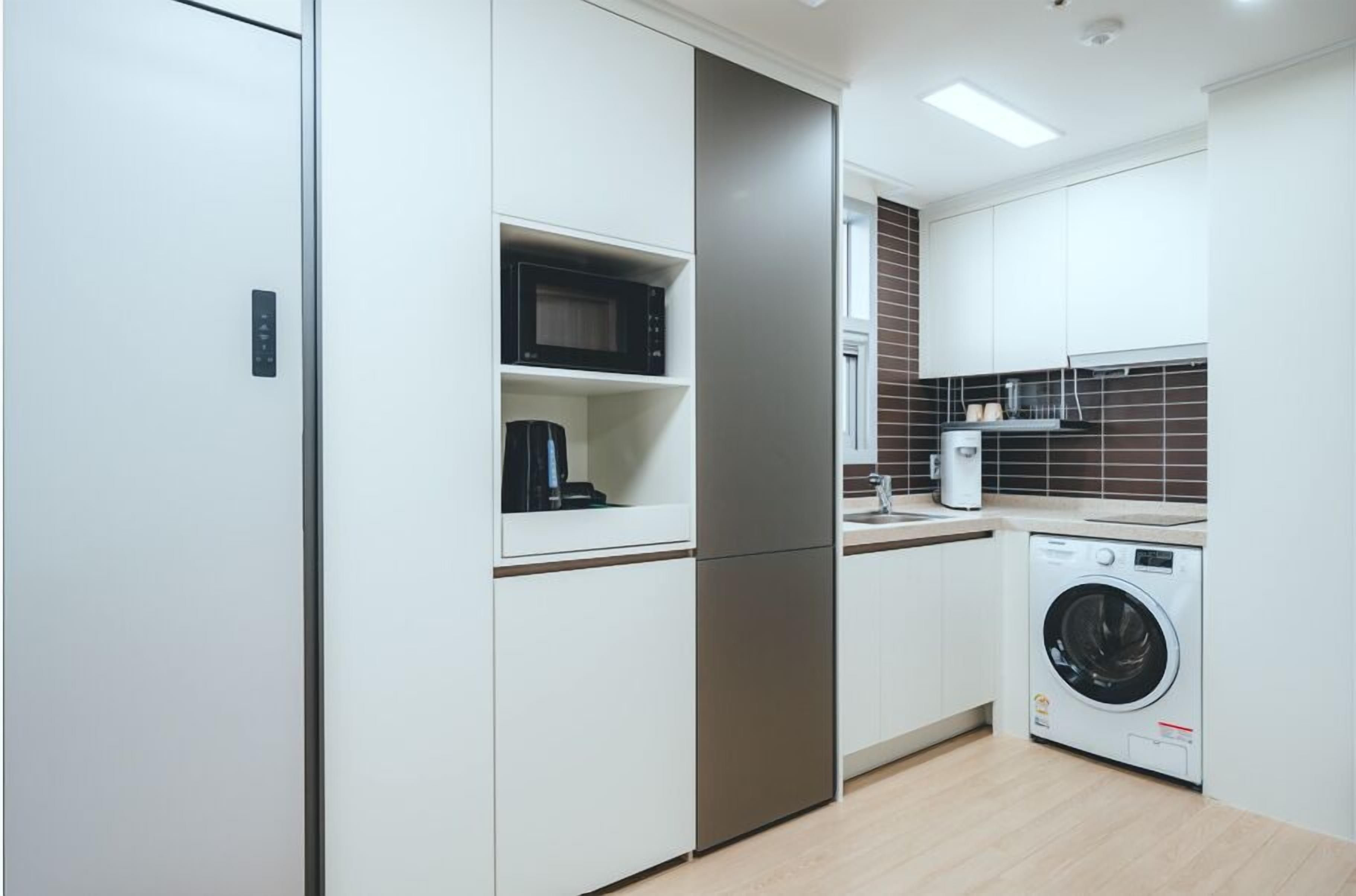 Une cuisine compacte avec des meubles blancs, un four à micro-ondes, une machine à café et un lave-linge.