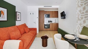 Una sala de estar moderna con un sofá, una mesa de comedor con platos y vasos, y una cocina al fondo.