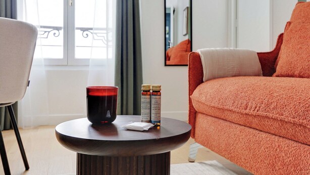 Una sala de estar moderna con una mesa redonda de madera, una vela roja y dos botellas de champú.