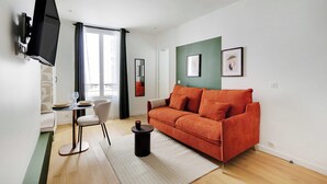 Una sala de estar moderna con un sofá, un televisor montado en la pared, un comedor con mesa y sillas, y un amplio ventanal con cortinas.