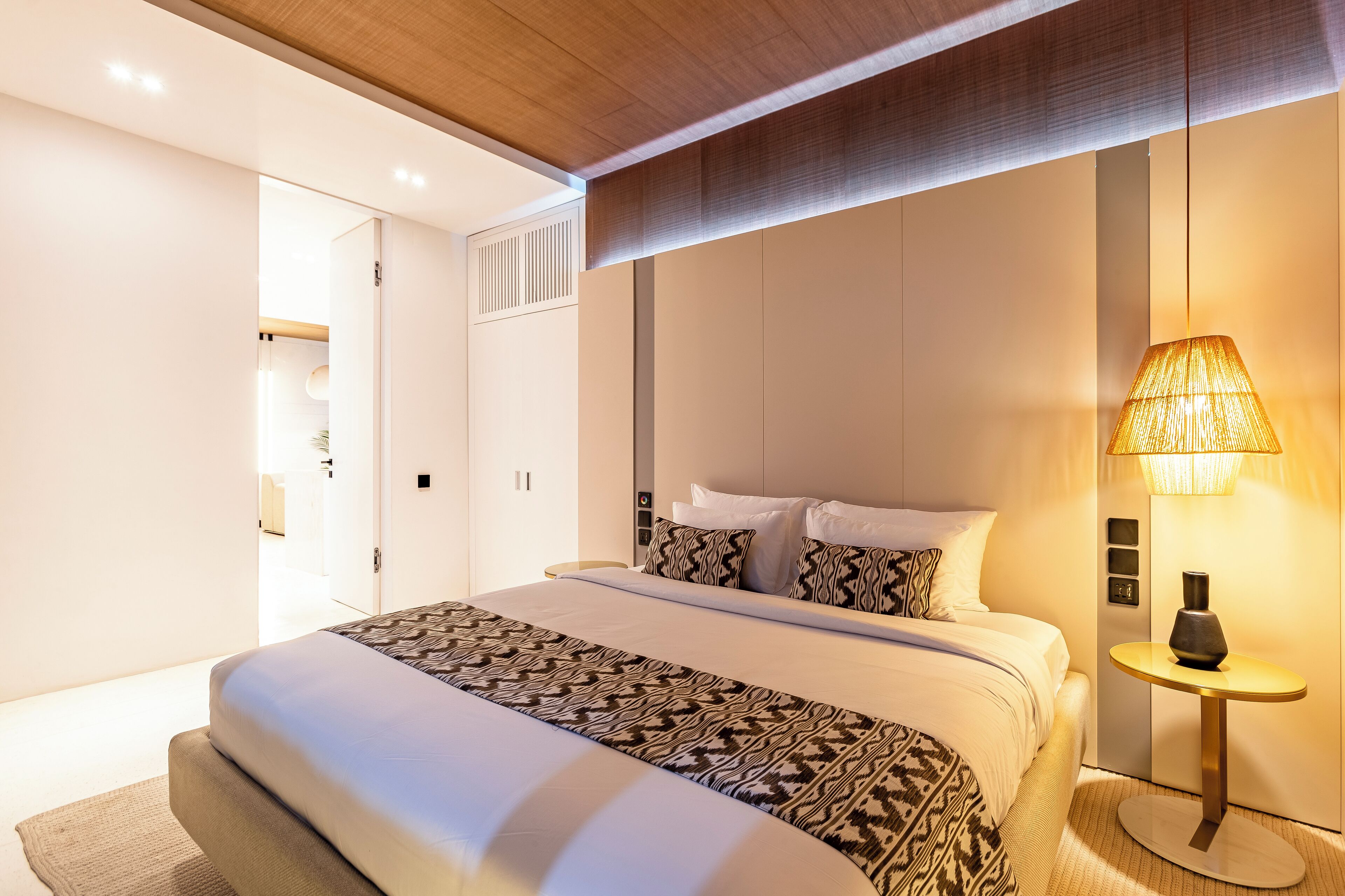 A modern bedroom with a large bed, a bedside table with a lamp, and a wardrobe.