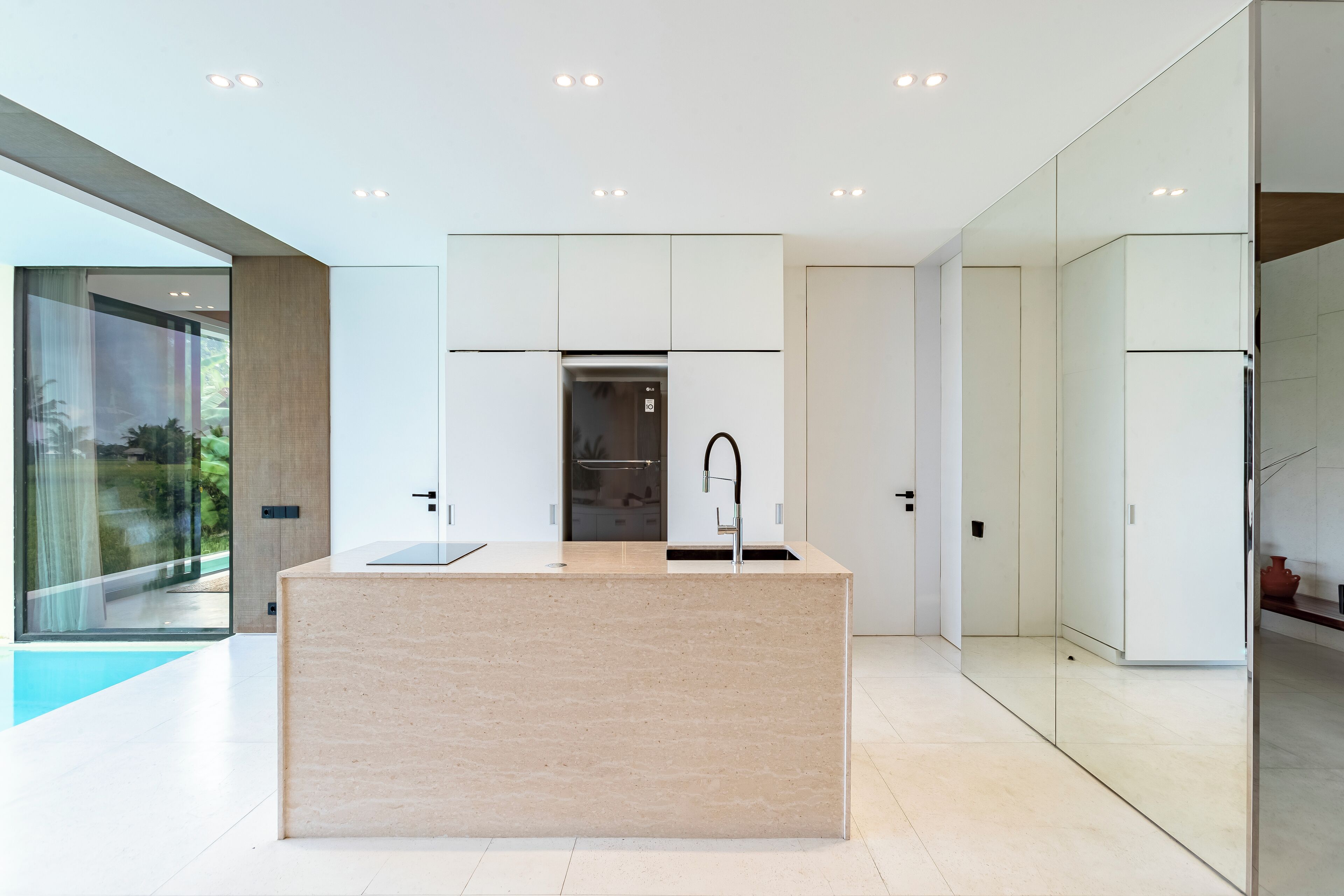 Una cocina moderna con una isla central, luces empotradas en el techo y vistas al exterior a través de amplios ventanales.