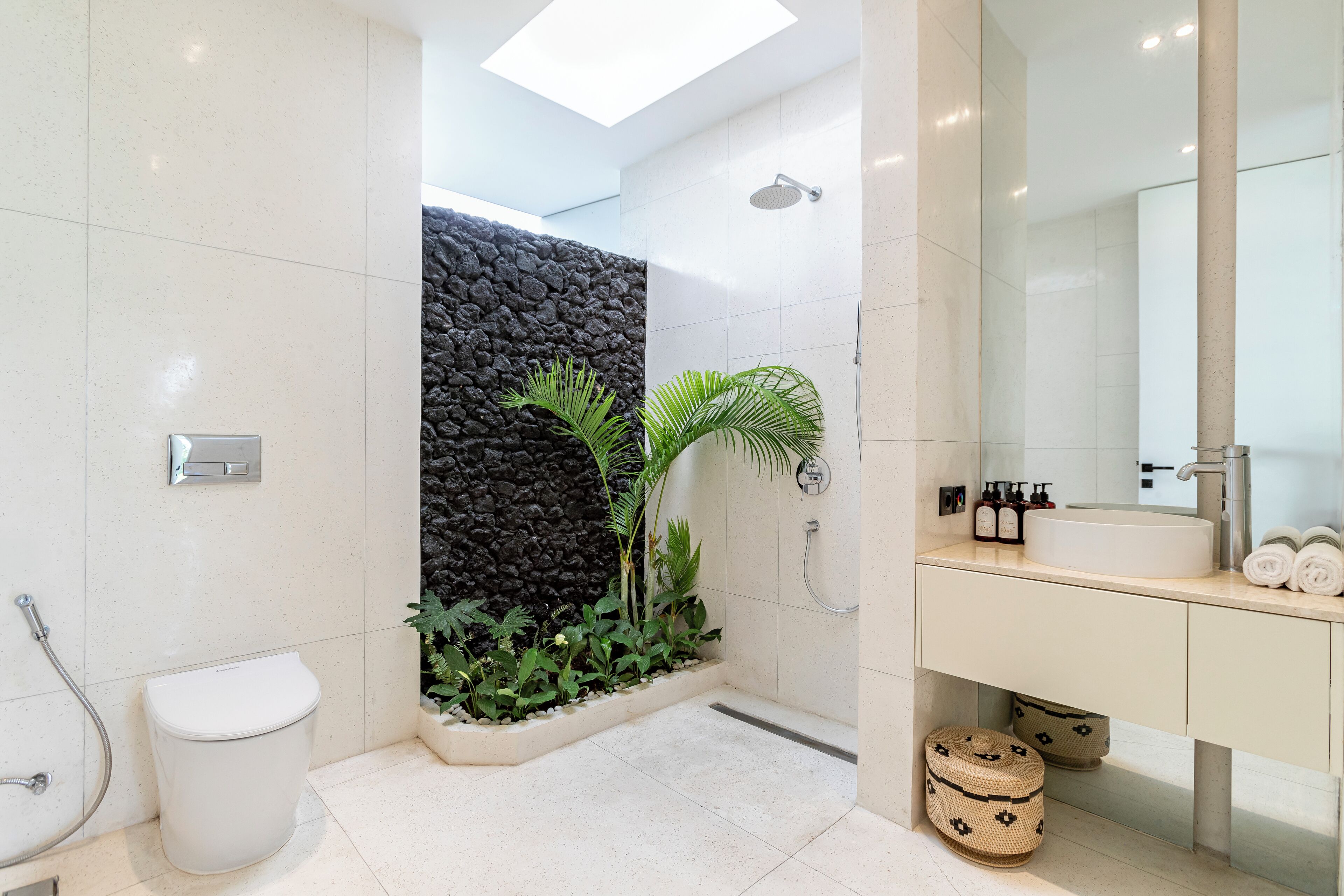 Een moderne badkamer met een wit toilet, een douche met een stenen muur en een wastafel met spiegel.