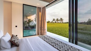 A modern bedroom with a large window, a bed with patterned bedding, and a view of a green field. - Azure 2BR Villa in Ubud Rice Field views (Ubud)