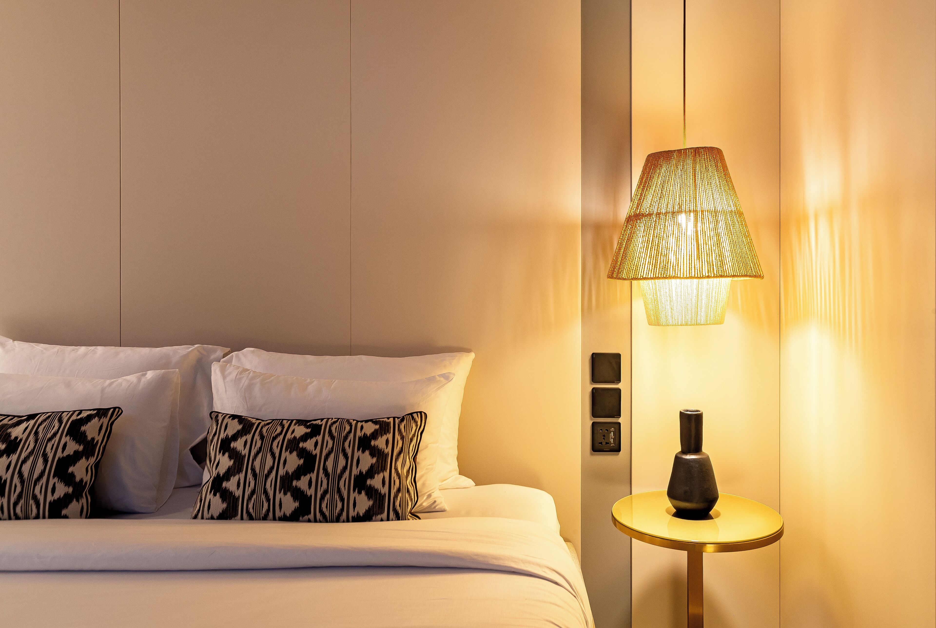 A hotel room with a bed, patterned pillows, a lamp, and a small table.
