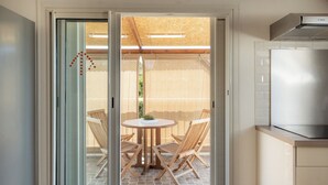 A kitchen with a Bosch refrigerator, a dining area with a round table and four wooden chairs, and a sliding glass door leading to an outdoor patio with a wooden pergola and a chair. - Résidence tamarin - nature lovers - sea and mountain views (LA RIVIERE)