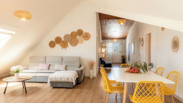 A modern living room with a sofa, coffee table, and yellow chairs. There is a dining area with a table and chairs. The room has wooden flooring and a sloped ceiling. - Résidence tamarin - nature lovers - sea and mountain views (LA RIVIERE)