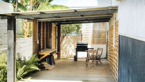 A covered patio with a grill, seating, and a wooden deck. - Résidence tamarin - nature lovers - sea and mountain views (LA RIVIERE)