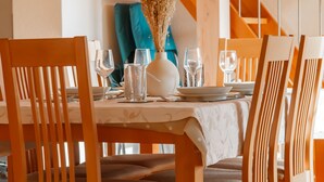 Une table à manger avec des chaises, un vase contenant des fleurs séchées et de la verrerie transparente.