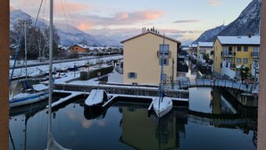 Un port de plaisance avec des bateaux amarrés, un immeuble doté de balcons et, au loin, des montagnes enneigées.