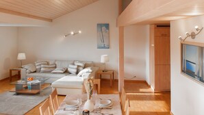 Un salon moderne avec un plafond haut, un ensemble de canapés, une table basse en verre et un coin repas avec une table dressée pour quatre personnes.