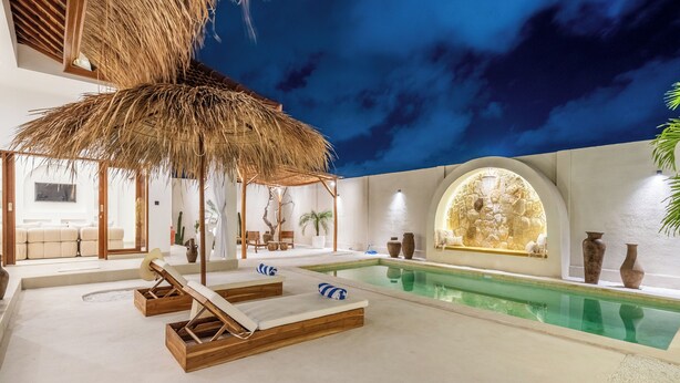 A pool area with lounge chairs, a thatched roof, and a decorative wall with vases. - THE LUXURY LIVING (Canggu)