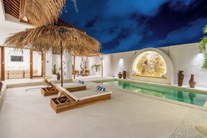 A pool area with lounge chairs, a thatched roof, and a decorative wall with vases. - THE LUXURY LIVING (Canggu)