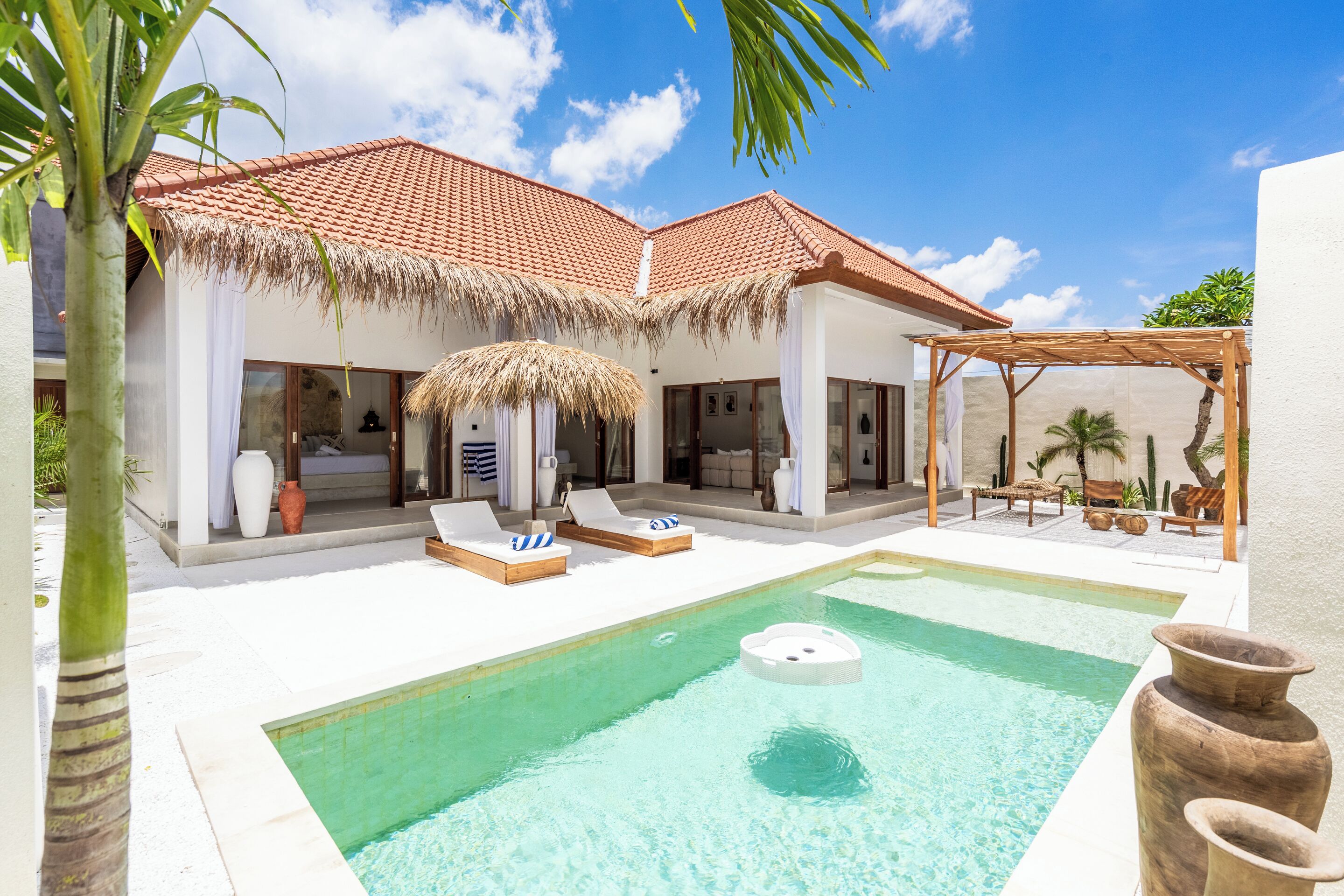 Un resort con piscina, sillas de descanso y una estructura de techo de paja.
