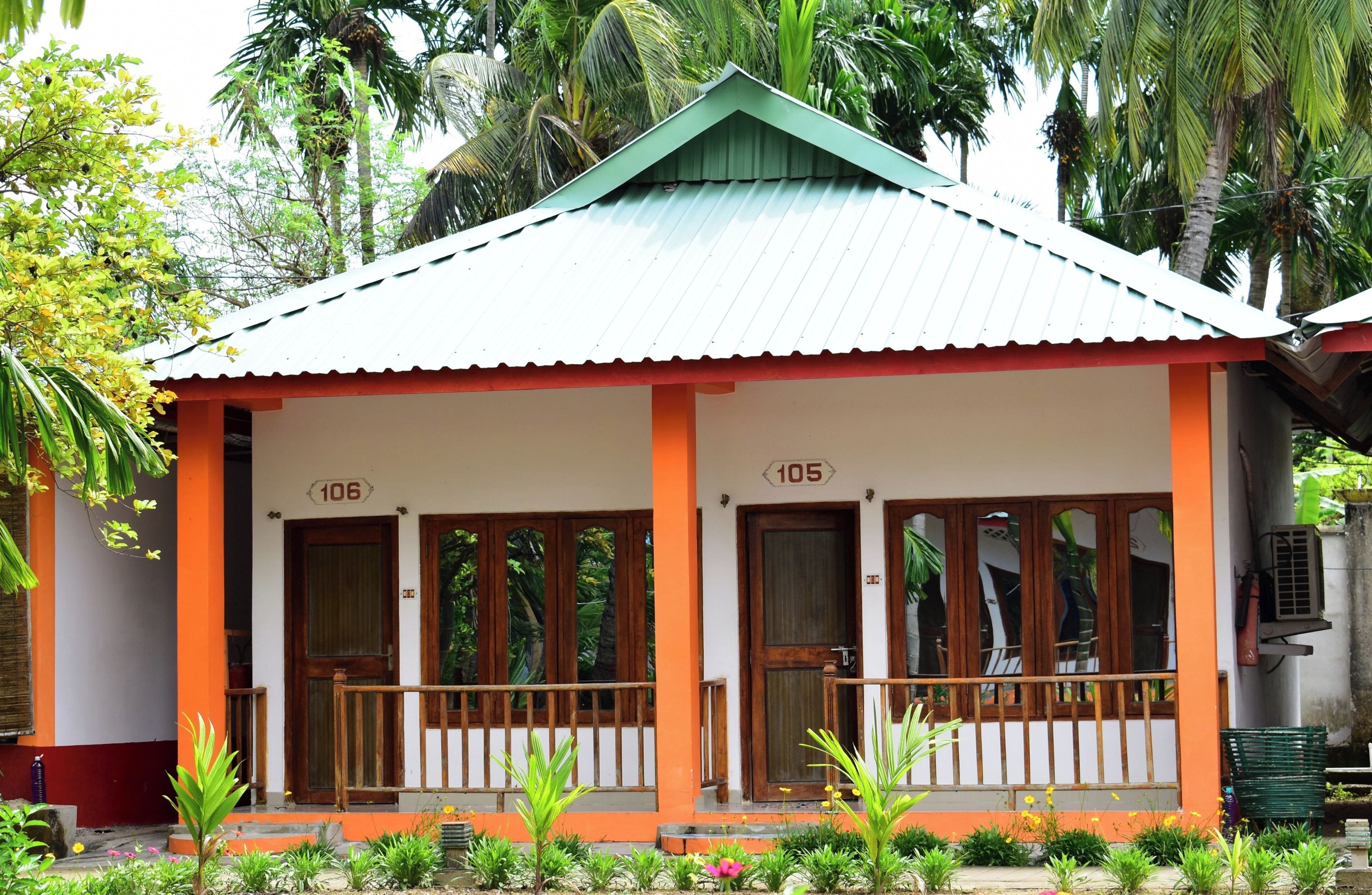 Un bâtiment à deux étages, doté d’un toit végétalisé et de touches de couleur orange, portant les numéros 105 et 106, et entouré d’une végétation luxuriante.