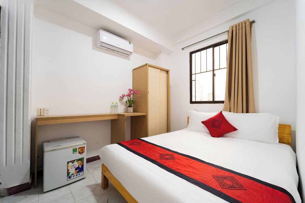 A hotel room with a bed, a desk, a wardrobe, and an air conditioning unit.