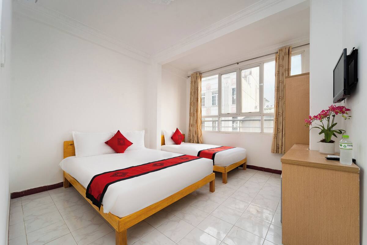 A hotel room with two beds, a wooden desk, a TV, and a window with curtains.