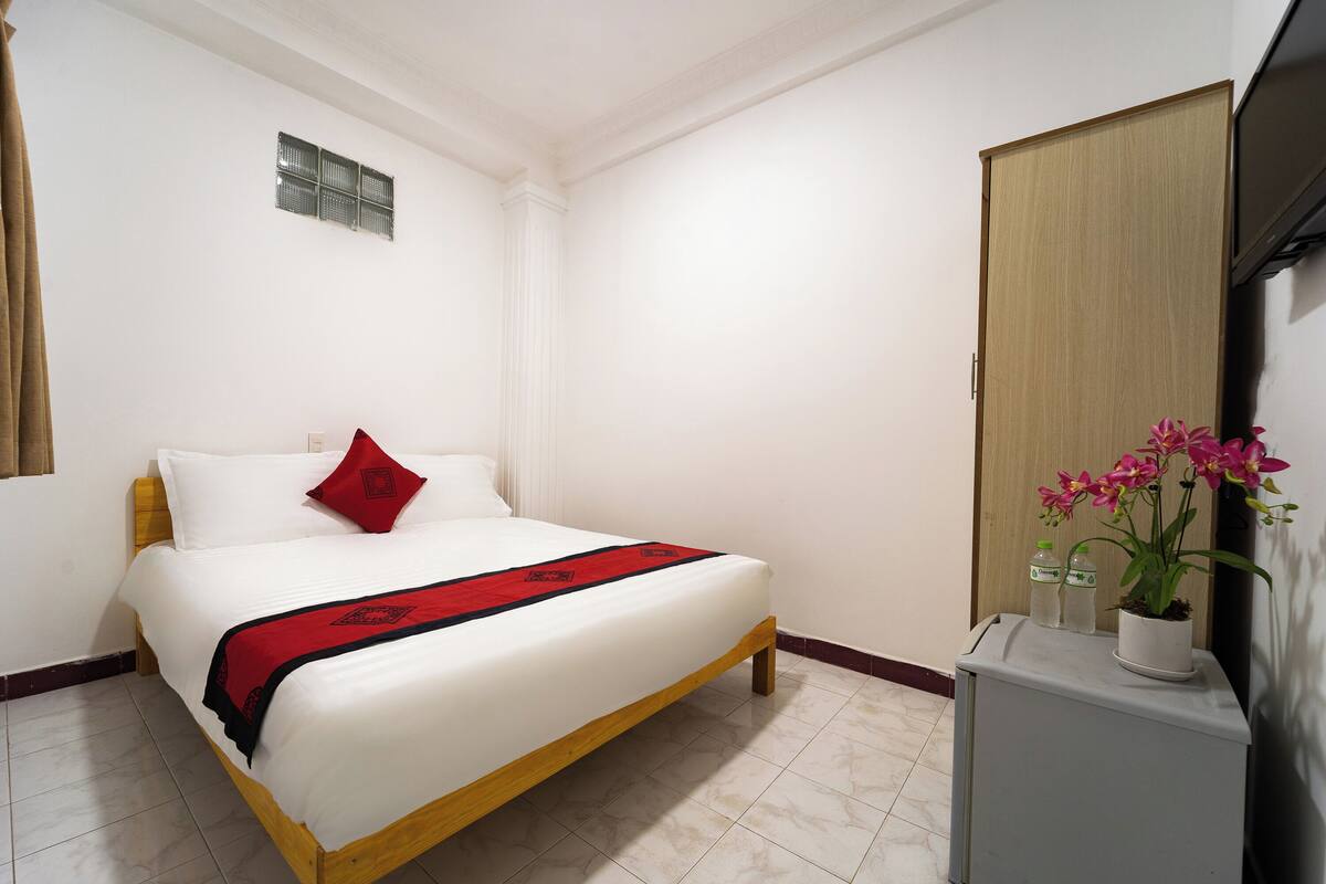 A hotel room with a bed, a small desk, a television, and a potted plant.