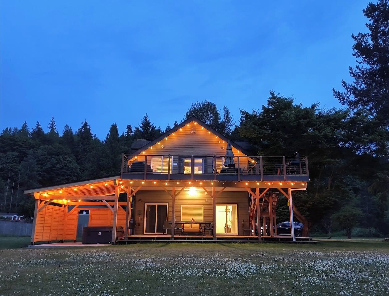 Una casa de madera de dos pisos con un balcón, luces colgantes y un porche cubierto.