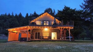 Ein zweistöckiges Holzhaus mit Balkon, Lichterkette und überdachter Veranda.