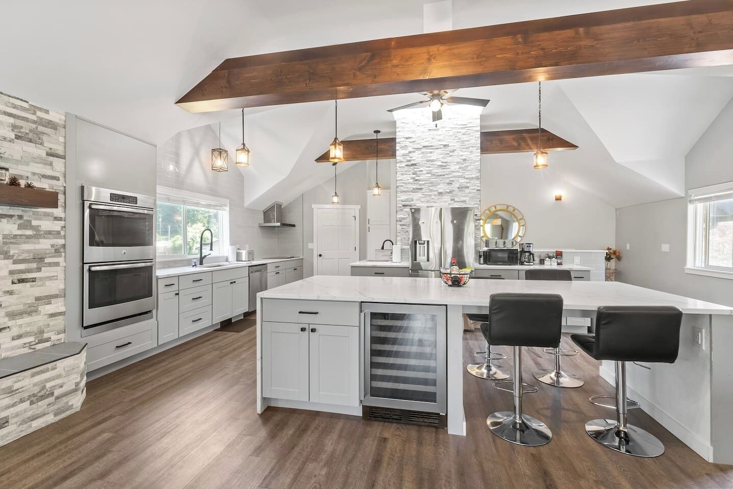 Una cocina moderna con armarios blancos, una isla grande con taburetes de bar y una viga de techo de madera.
