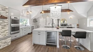 Eine moderne Küche mit weißen Schränken, einer großen Kochinsel mit Barhocker und einem Holzbalken an der Decke.