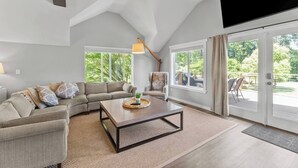 Ein geräumiges Wohnzimmer mit einer großen Couch, einem Couchtisch und Blick ins Freie durch große Fenster.