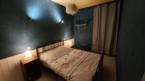 Ein Schlafzimmer mit einem Bett, zwei Nachttischen mit Lampen, einem Holzkopfteil, einer Ablage mit einer Vase und einem Vorhang.