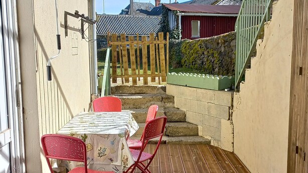 Eine Holzterrasse mit Tisch, Stühlen und Blick auf angrenzende Gebäude.