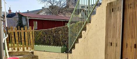 Une terrasse en bois avec une table et des chaises, un escalier et une vue sur le clocher d’une église.
