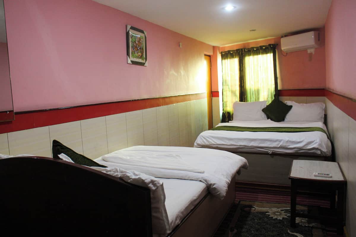 A hotel room with two beds, a small table, and a window with curtains.