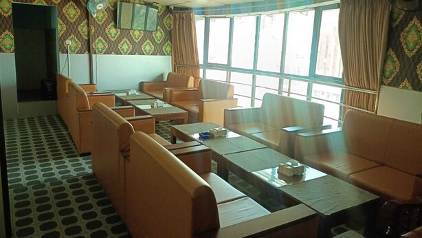 A room with a patterned wallpaper, a television, a large window with curtains, and a seating area with tables and chairs. - Vibor Hotel  (Kathmandu)