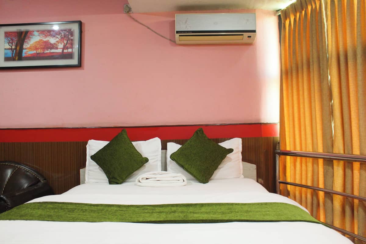 A hotel room with a bed, a picture on the wall, an air conditioner, and a curtain.