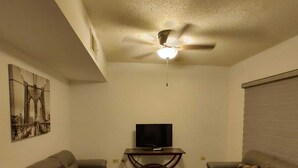 A living room with two sofas, a TV on a stand, and a ceiling fan.