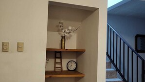 A staircase with a black railing, a clock on the wall, and a vase with flowers on a shelf.