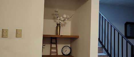 Uma escadaria com corrimão preto, um relógio na parede e um vaso com flores em uma prateleira.