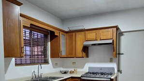 A kitchen with wooden cabinets, a gas stove, a sink, and a window with blinds.