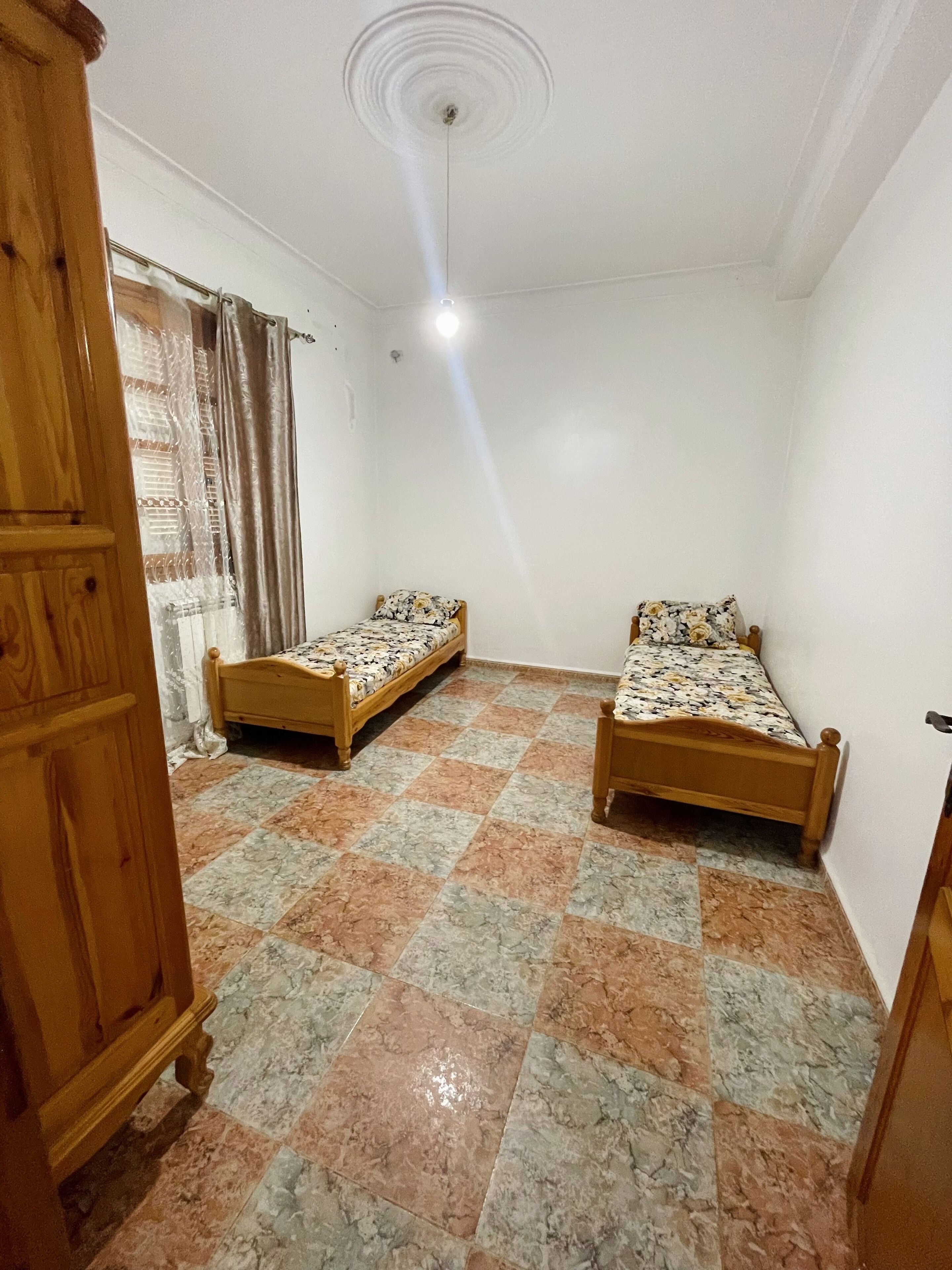 Una habitación con dos camas de madera, un armario de madera y suelo de baldosas.