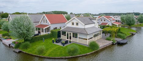 A row of houses with a river in the foreground, featuring a grassy lawn and outdoor seating area.