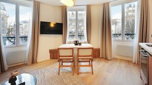 A modern living room with a dining table, two chairs, a flat-screen TV, and large windows with curtains. - Elegant Apartment - 1br/4p - Sacre-coeur (Paris)